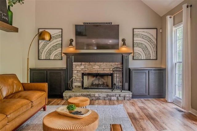living area featuring vaulted ceiling, a fireplace, visible vents, and wood finished floors