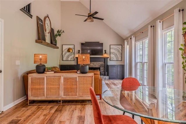 dining space featuring wood finished floors, high vaulted ceiling, a fireplace, a ceiling fan, and baseboards