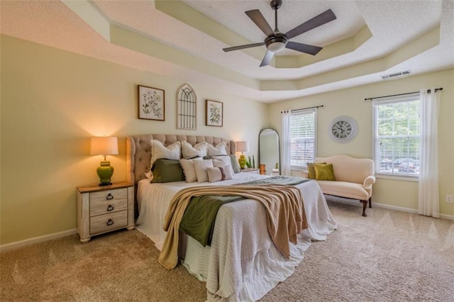 carpeted bedroom featuring a tray ceiling, baseboards, a ceiling fan, and visible vents