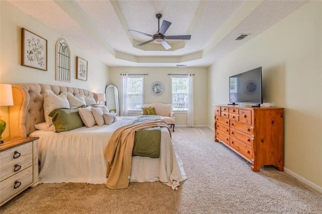 bedroom with light colored carpet, visible vents, baseboards, and a tray ceiling