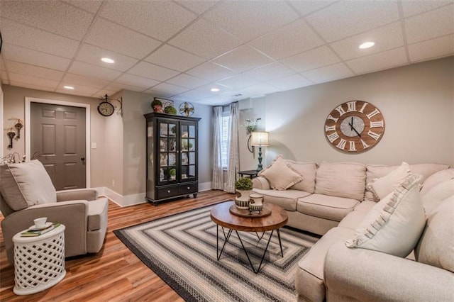 living room with a drop ceiling, wood finished floors, baseboards, and recessed lighting