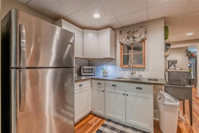 kitchen featuring a sink, freestanding refrigerator, a paneled ceiling, white cabinetry, and light wood-style floors