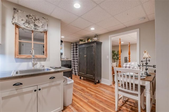 kitchen with a sink, light wood finished floors, white cabinetry, and a drop ceiling