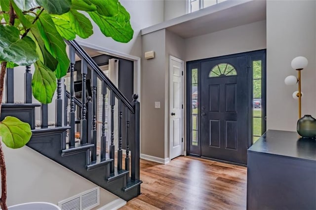foyer entrance featuring a wealth of natural light, stairway, visible vents, and wood finished floors
