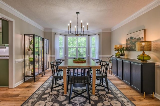 dining space featuring ornamental molding, light wood-style flooring, a chandelier, and a textured ceiling