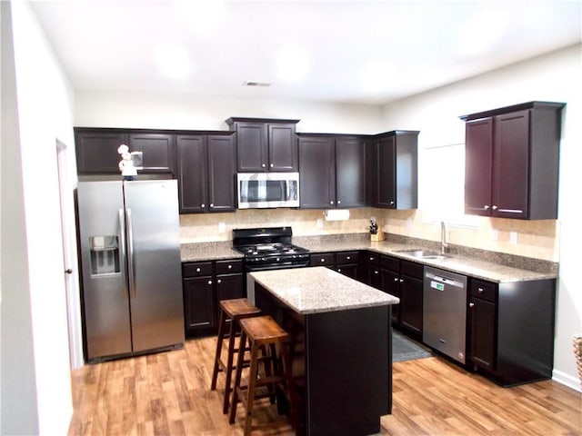 kitchen featuring appliances with stainless steel finishes, a center island, a breakfast bar, sink, and light hardwood / wood-style flooring