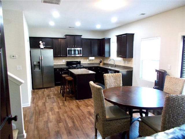 kitchen featuring a breakfast bar area, wood-type flooring, stainless steel appliances, a center island, and sink