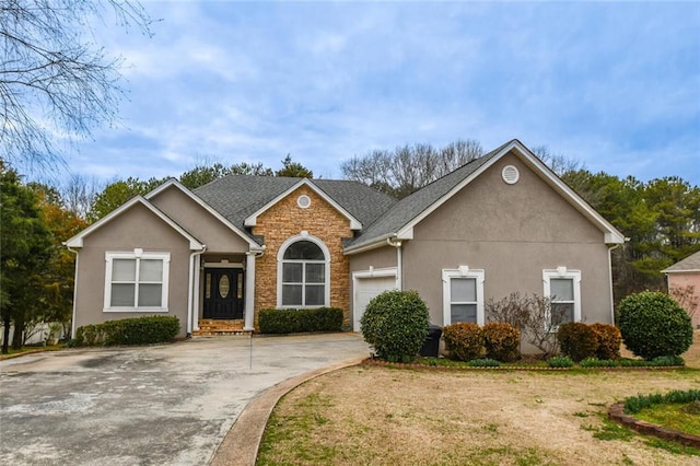 view of front facade featuring stone siding, driveway, an attached garage, and stucco siding