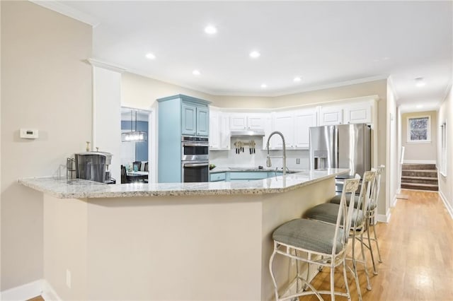 kitchen with kitchen peninsula, appliances with stainless steel finishes, light hardwood / wood-style floors, and crown molding