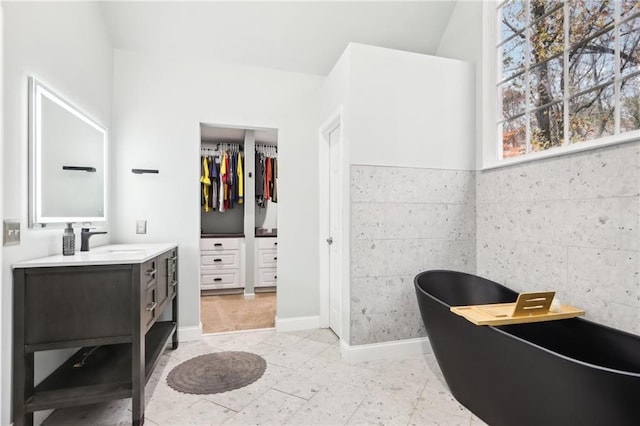 interior space with vanity, vaulted ceiling, a bath, tile walls, and tile patterned flooring