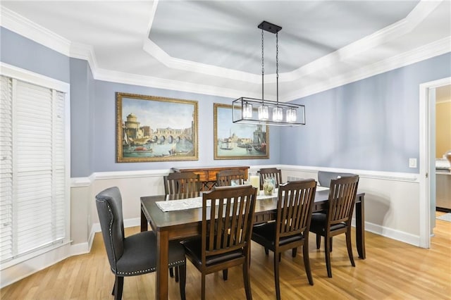 dining room featuring a raised ceiling, crown molding, and light hardwood / wood-style flooring