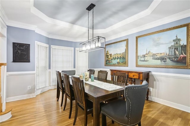 dining area with a raised ceiling, wood-type flooring, and ornamental molding