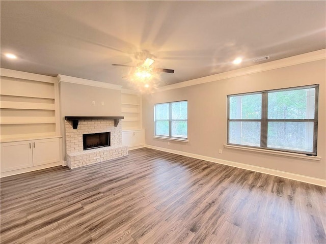 unfurnished living room featuring hardwood / wood-style floors, crown molding, a fireplace, built in features, and ceiling fan