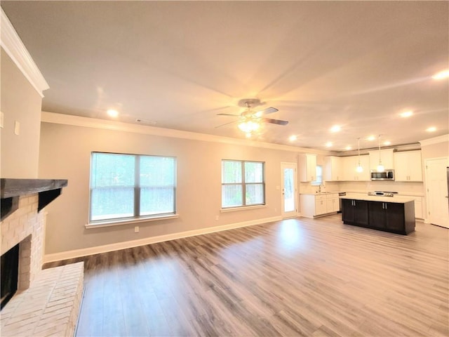 unfurnished living room featuring a brick fireplace, light hardwood / wood-style floors, ornamental molding, and ceiling fan