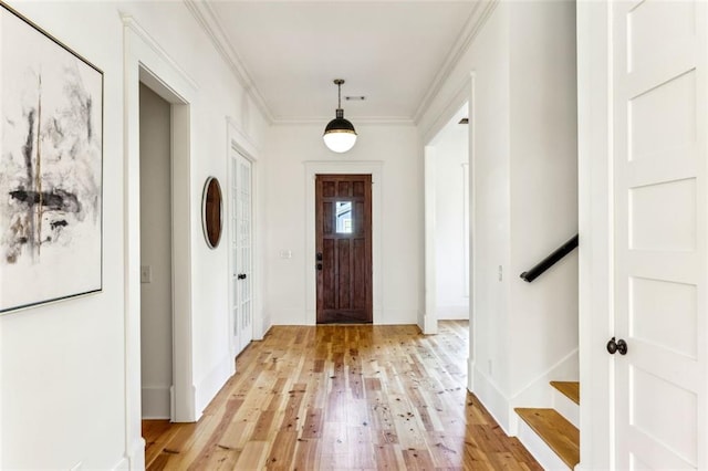 entryway with ornamental molding, light wood-type flooring, baseboards, and stairs