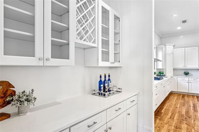 bar with light wood-style flooring, under cabinet range hood, white gas stovetop, visible vents, and crown molding