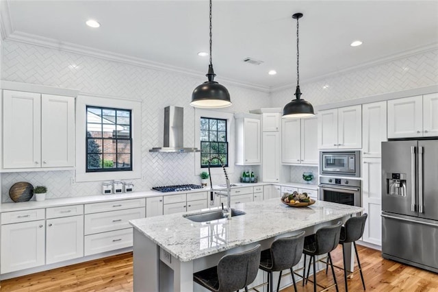 kitchen with stainless steel appliances, a sink, white cabinetry, wall chimney range hood, and crown molding