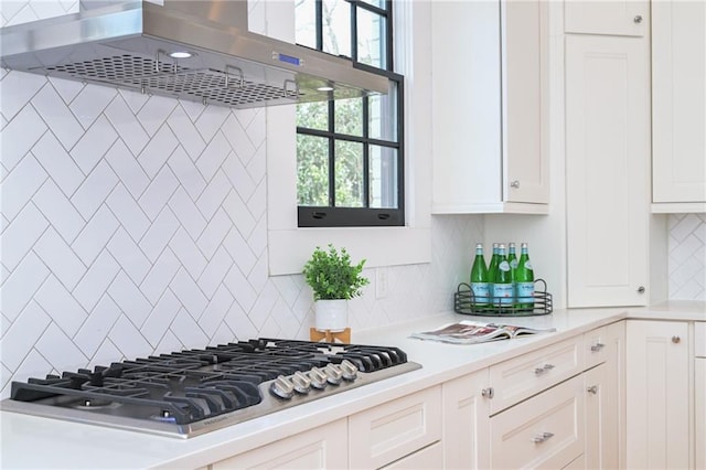 kitchen with white cabinets, light countertops, wall chimney range hood, stainless steel gas cooktop, and backsplash