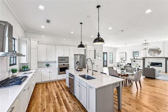 kitchen featuring a fireplace, stainless steel appliances, open floor plan, a sink, and wall chimney range hood