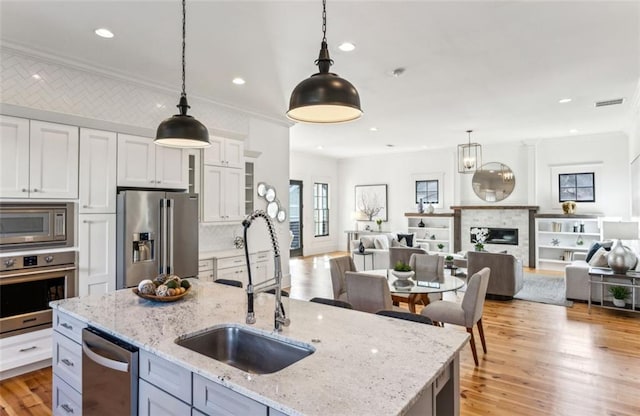 kitchen featuring stainless steel appliances, a fireplace, a sink, light wood-style floors, and open floor plan