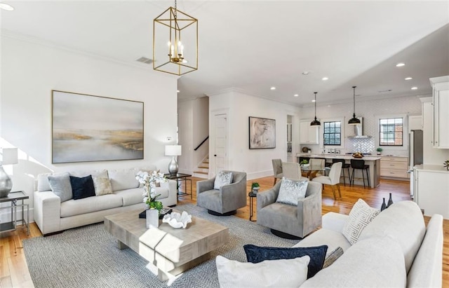 living area with light wood finished floors, stairway, a chandelier, and ornamental molding