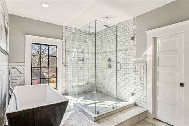 full bath featuring a stall shower, a soaking tub, a sink, and tile walls