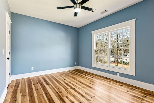 empty room featuring a ceiling fan, visible vents, baseboards, and wood finished floors