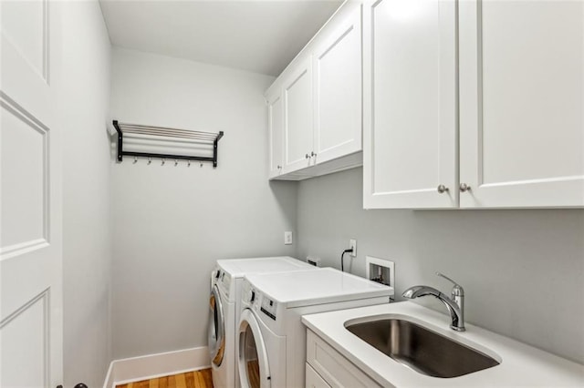 laundry room with washing machine and dryer, wood finished floors, a sink, baseboards, and cabinet space