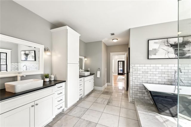 full bath with tasteful backsplash, two vanities, visible vents, a sink, and a freestanding tub