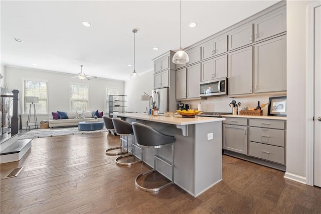 kitchen with a center island with sink, stainless steel appliances, hanging light fixtures, and gray cabinets