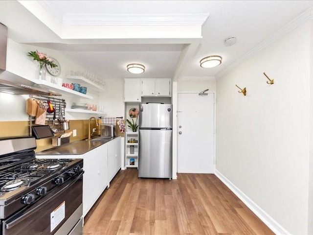 kitchen with light wood-type flooring, ornamental molding, gas range oven, freestanding refrigerator, and a sink