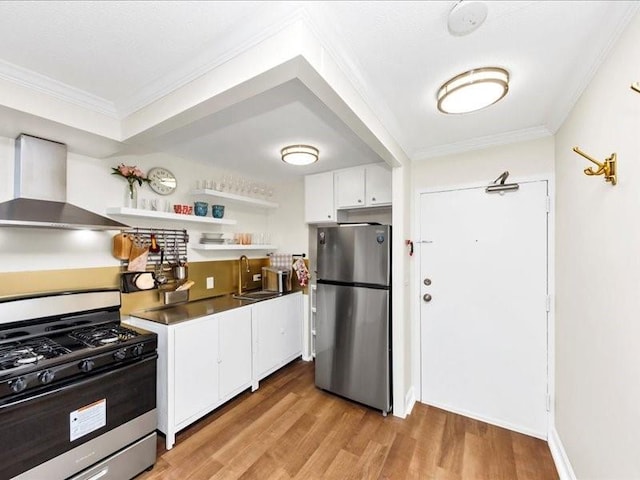 kitchen featuring crown molding, wall chimney range hood, stainless steel appliances, white cabinetry, and a sink