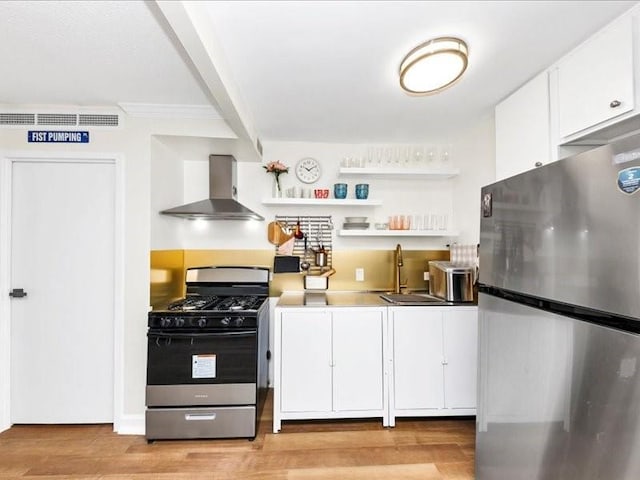 kitchen featuring light wood finished floors, a sink, stainless steel appliances, white cabinets, and wall chimney range hood