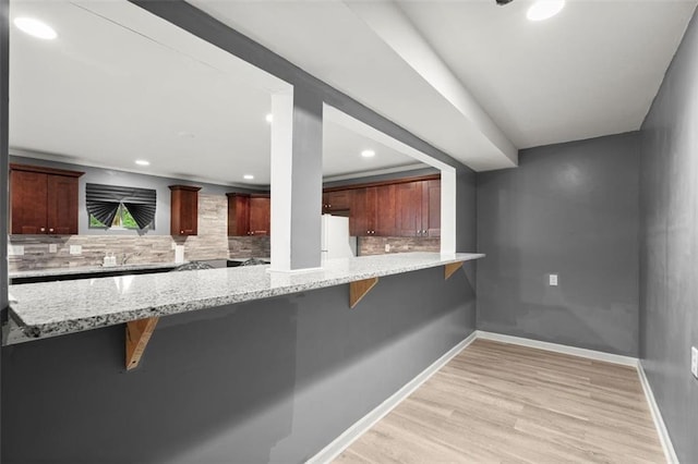 1709 Grove Ct SE, Conyers, GA 30013 - kitchen with freestanding refrigerator, light wood-style floors, a breakfast bar area, backsplash, and light stone countertops