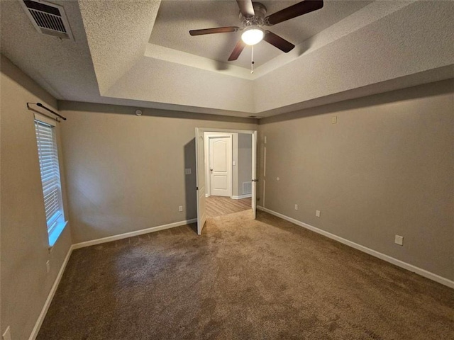 unfurnished bedroom with ceiling fan, multiple windows, a raised ceiling, and carpet