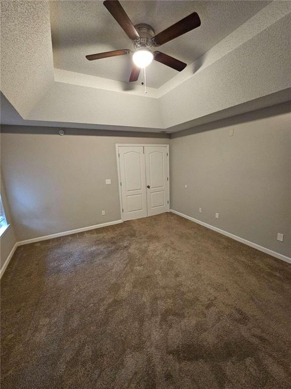 unfurnished bedroom featuring carpet, a textured ceiling, ceiling fan, and a tray ceiling