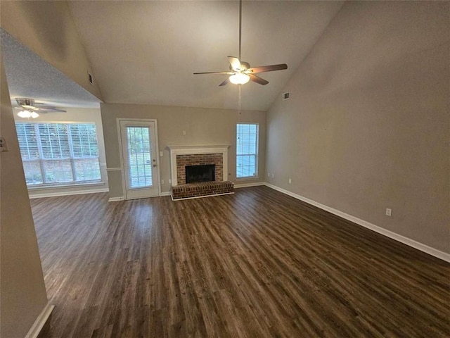 unfurnished living room featuring ceiling fan, a wealth of natural light, dark hardwood / wood-style floors, and a brick fireplace