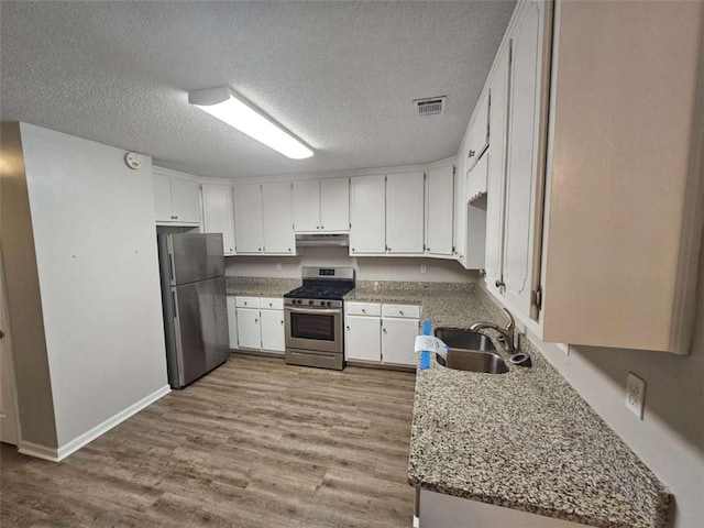 kitchen with stainless steel appliances, light stone counters, white cabinets, sink, and light wood-type flooring