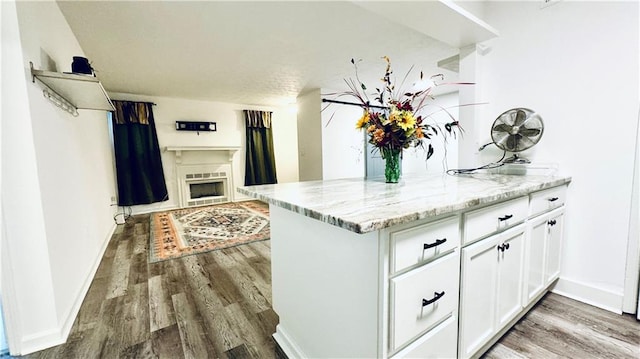 kitchen with white cabinets, dark hardwood / wood-style floors, light stone countertops, and kitchen peninsula