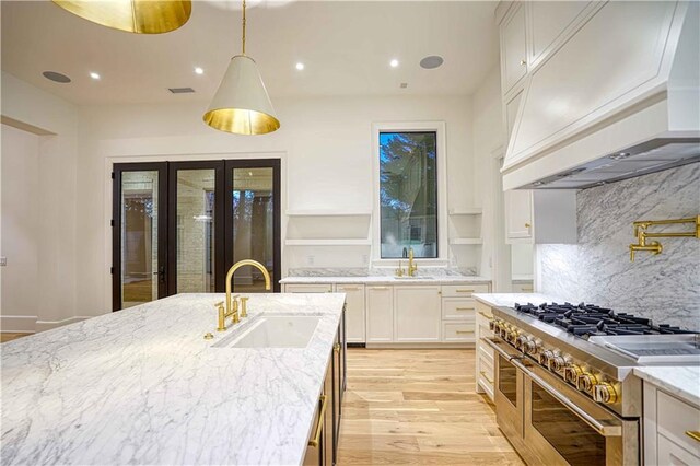 kitchen with light stone counters, backsplash, sink, range with two ovens, and custom exhaust hood