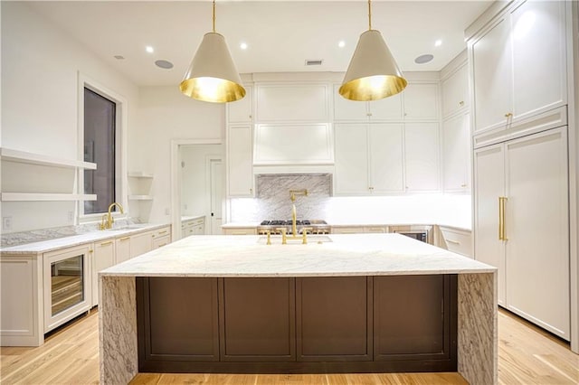 kitchen featuring pendant lighting, an island with sink, white cabinetry, light wood-type flooring, and wine cooler