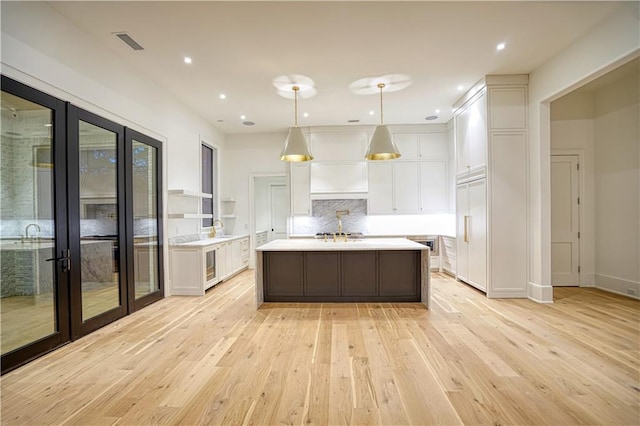 kitchen with white cabinetry, pendant lighting, an island with sink, and light hardwood / wood-style floors