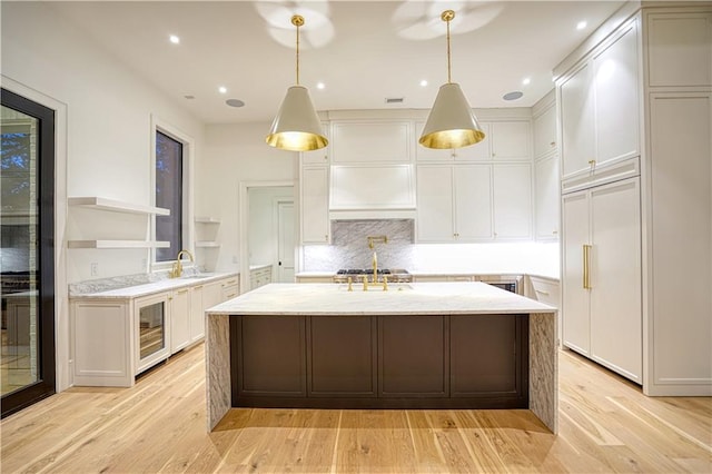 kitchen with light stone countertops, hanging light fixtures, light hardwood / wood-style floors, and white cabinets