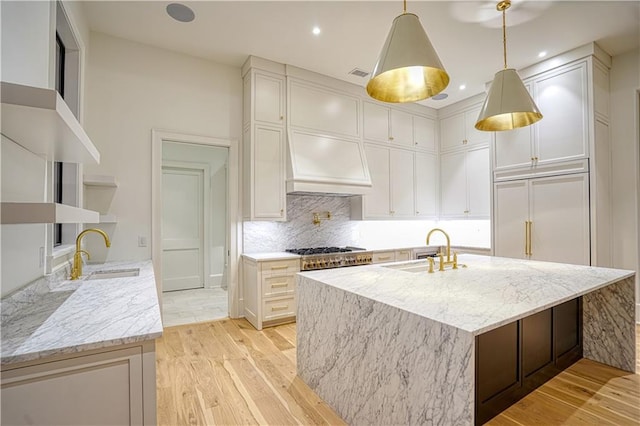 kitchen featuring light stone countertops, a center island with sink, sink, and light hardwood / wood-style floors