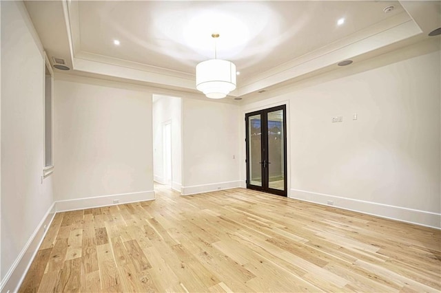 empty room with a tray ceiling, french doors, and light hardwood / wood-style floors