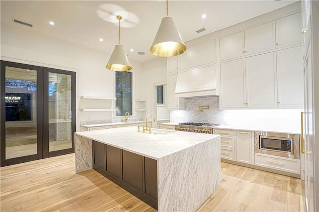 kitchen with white cabinetry, sink, light stone countertops, a kitchen island with sink, and light wood-type flooring