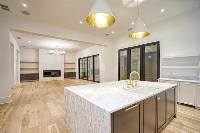 kitchen featuring light stone counters, sink, white cabinetry, light wood-type flooring, and decorative light fixtures