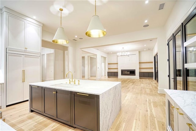 kitchen with white cabinets, sink, light stone countertops, light wood-type flooring, and decorative light fixtures