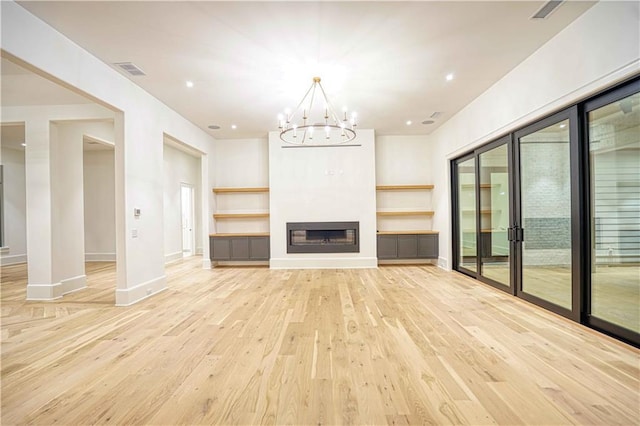 unfurnished living room with a wealth of natural light, light hardwood / wood-style flooring, and an inviting chandelier