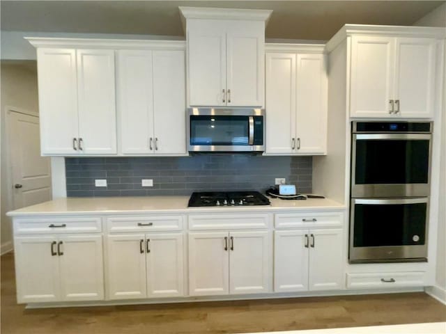 kitchen with backsplash, appliances with stainless steel finishes, light hardwood / wood-style floors, and white cabinets